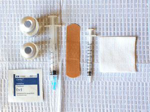 Photo is of medical supplies including two needles and two vials of hormones. 