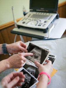 Photo is of the hands of two people holding an ultrasound photo.