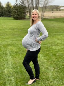 Very-pregnant Hope smiles while standing on a green, grassy lawn.
